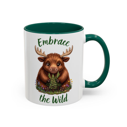 A white ceramic mug with a dark green handle and interior, featuring a printed illustration of a brown moose holding a pine tree, with the words 'Embrace the Wild' in green script.